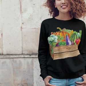 May include: Black sweatshirt with a colorful illustration of a wooden crate filled with fresh produce, including a pumpkin, watermelon, eggplant, and various leafy greens.