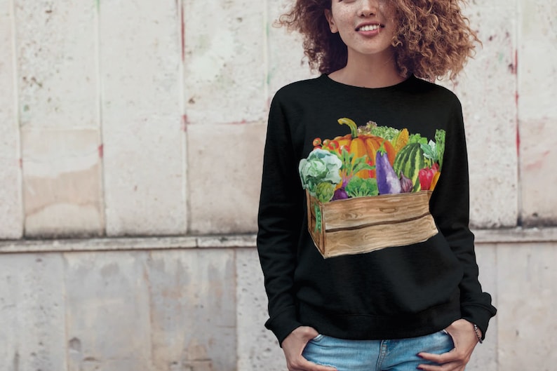 May include: Black sweatshirt with a colorful illustration of a wooden crate filled with fresh produce, including a pumpkin, watermelon, eggplant, and various leafy greens.
