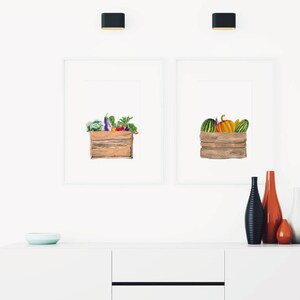 May include: Two framed watercolor illustrations of wooden crates filled with produce. The left crate is filled with vegetables, including eggplant, broccoli, and peppers. The right crate is filled with pumpkins and gourds.