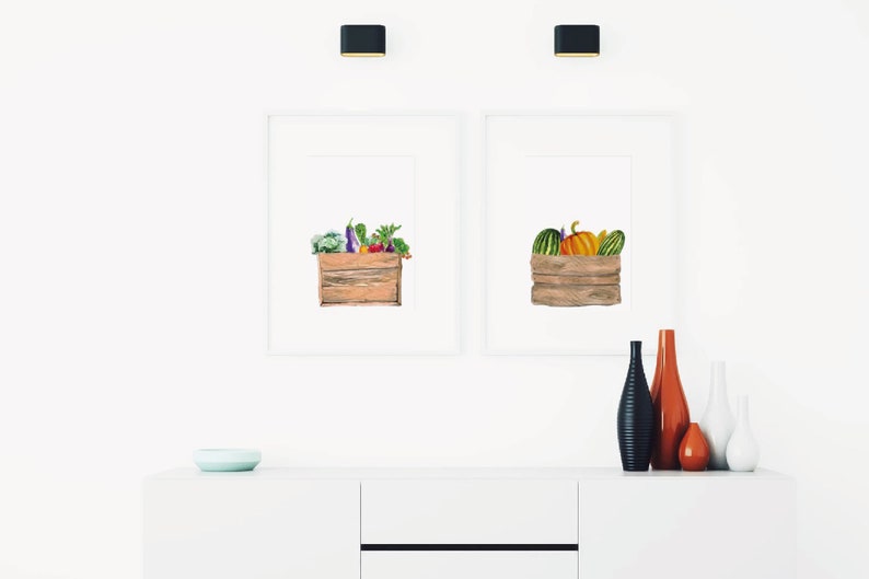 May include: Two framed watercolor illustrations of wooden crates filled with produce. The left crate is filled with vegetables, including eggplant, broccoli, and peppers. The right crate is filled with pumpkins and gourds.