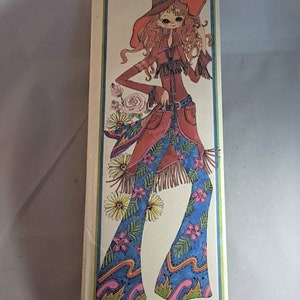 May include: A vintage memo pad cover featuring a colorful illustration of a woman wearing a red cowboy hat, a red jacket, and blue bell-bottom pants with a floral pattern. The text "Memo Pads" is printed in pink and white.