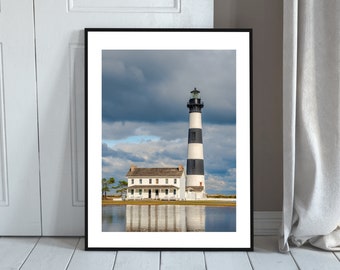 May include: A black and white striped lighthouse with a white house in front of it. The lighthouse is tall and slender, and the house is small and quaint. The sky is cloudy and dramatic, and the water is calm and reflective.