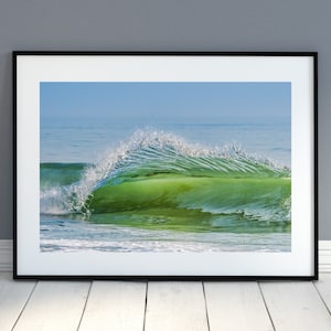 May include: A photograph of a green wave crashing on a beach. The wave is breaking into a spray of white water. The water is clear and blue.