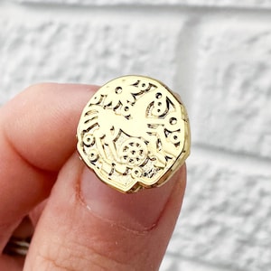 Può includere: Un anello d'oro con un design dettagliato e intricato. L'anello è di forma ovale e ha una superficie testurizzata.
