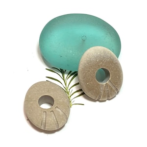 May include: Three smooth, round stones with holes in the center. Two of the stones are light brown and one is a light turquoise blue.