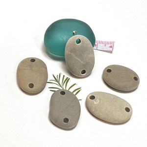 May include: Five natural stone oval pendants with two holes each. The stones are a light brown color and have a smooth, polished finish.