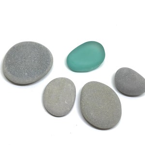 May include: Five smooth stones, four gray and one light blue, arranged on a white surface.