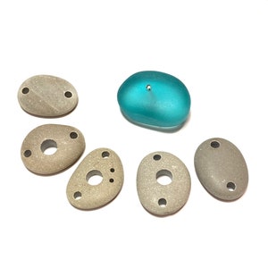 May include: Six smooth, gray stones with various shapes and holes, and one teal blue glass stone.