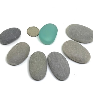 May include: Seven smooth, oval-shaped stones in shades of gray, with one light blue glass stone in the center.