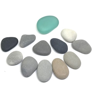 May include: A collection of smooth, gray and white stones, with one light green glass stone. The stones are arranged in a circle on a white background.