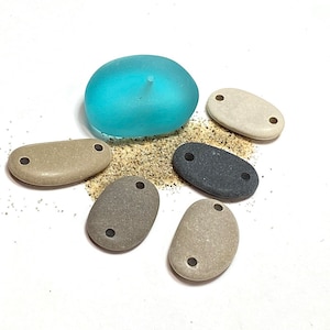 May include: Six smooth, oval-shaped stones with holes drilled through them. The stones are various shades of brown and gray, and one is a light blue color.