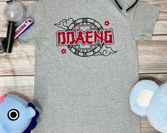 May include: Gray t-shirt with a red and black graphic design featuring a clock with the word "DDAENG" inside. The design is surrounded by clouds and flowers.