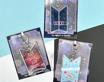 May include: Three different BTS keychain designs. The first keychain is a black and blue design with the text "00:00". The second keychain is a colorful design with the text "You were the right". The third keychain is a light blue design with white flowers and white sneakers.