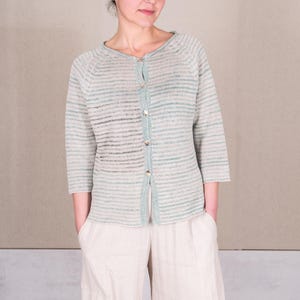 Puede incluir: Un cárdigan a rayas azul claro y blanco con cierre de botones. El cárdigan tiene un corte holgado y está hecho de una tela suave y ligera.