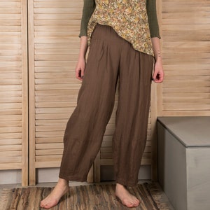 Pode incluir: Uma mulher vestindo um top marrom com estampa floral, gola verde e mangas compridas, combinado com calças largas marrons.