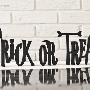 May include: Black wooden cutout letters spelling "Trick or Treat" on a white brick background.