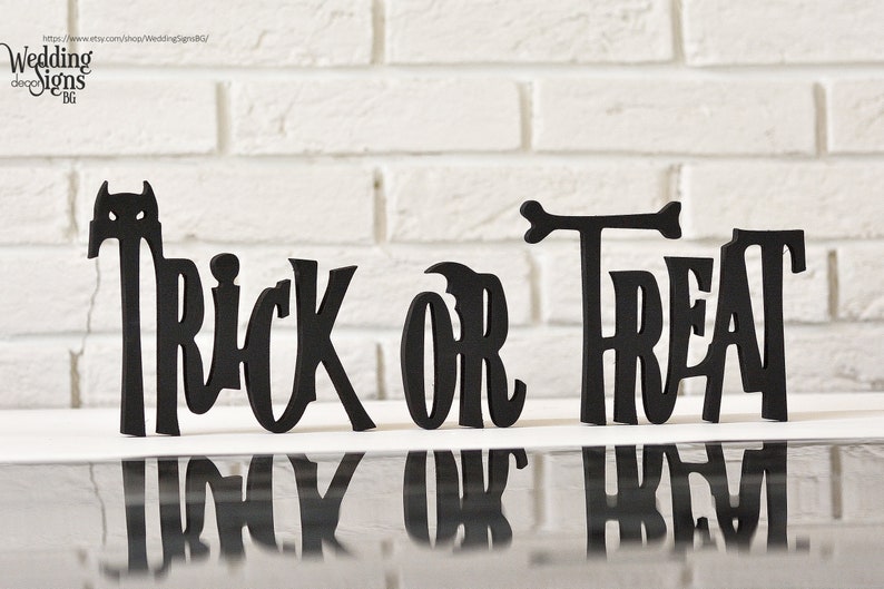 May include: Black wooden cutout letters spelling "Trick or Treat" on a white brick background.