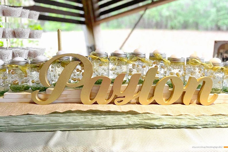 Multiple personalized name signs in gold finish displayed outdoors, garden party Quinceañera decor