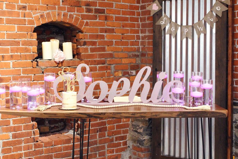 Large custom wooden name sign in rose gold finish on brick wall background, freestanding mis quince decor