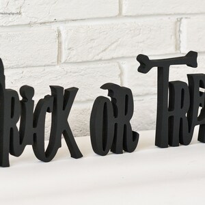 May include: Black wooden cutout letters spelling "Trick or Treat" with a small arrow above the "T" in "Treat".