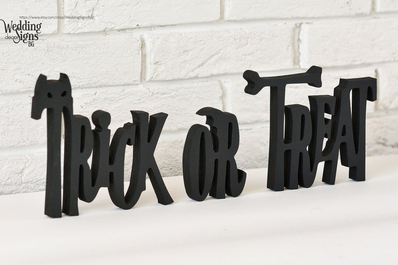 May include: Black wooden cutout letters spelling "Trick or Treat" with a small arrow above the "T" in "Treat".