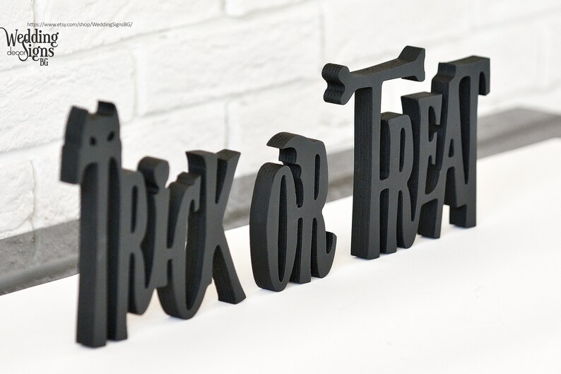 May include: Black wooden letters spelling out "Trick or Treat" in a decorative font. The letters are freestanding and can be used for Halloween decorations.