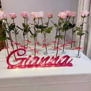 Custom wooden name sign in red glitter finish with pink roses on white table, Quinceañera gift keepsake