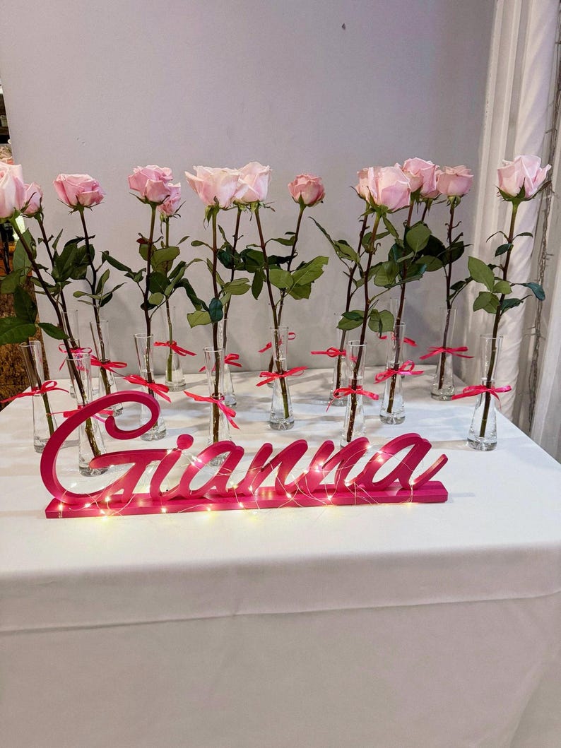 Custom wooden name sign in red glitter finish with pink roses on white table, Quinceañera gift keepsake