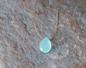 May include: A delicate gold chain necklace with a light blue teardrop-shaped gemstone pendant.