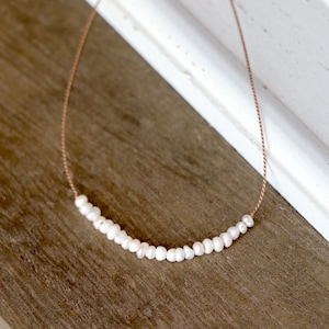 Puede incluir: Un collar delicado con una sola hebra de pequeñas perlas blancas en un cordón fino marrón.