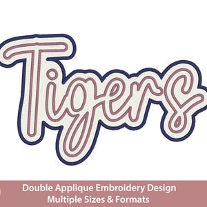 May include: An embroidery design featuring the word Tigers in a cursive script font. The lettering has a dusty rose center, a white middle layer, and a dark navy blue outer border. The text Hand Digitized is visible in a gold circular emblem.