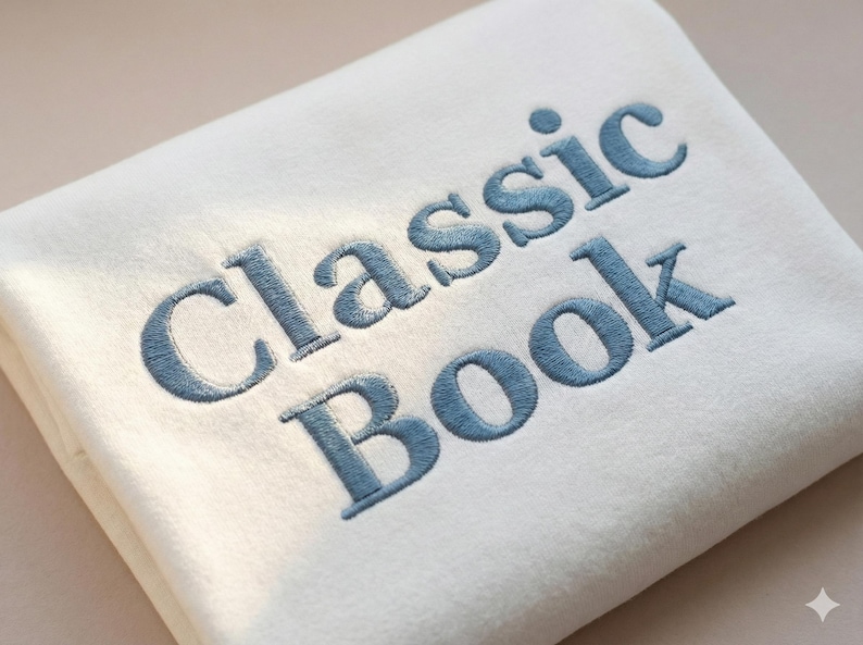May include: A folded, off-white blanket with the words "Classic Book" embroidered in a light blue thread. The text is in a serif font and is centered on the blanket.