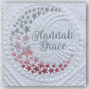 May include: White quilted baby blanket with a crescent moon design embroidered with silver and pink stars. The name "Hannah Grace" is embroidered in silver thread in the center of the moon.