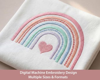 May include: A white fabric square featuring a machine-embroidered rainbow design with pastel pink, orange, light blue, green, and lavender arches. A small, solid pink embroidered heart is centered beneath the rainbow arches.
