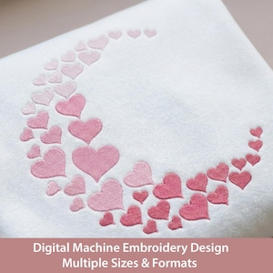 Puede incluir: Una superficie de tela blanca con forma de media luna compuesta por numerosos corazones bordados en varios tonos de rosa. El texto Digital Machine Embroidery Design Multiple Sizes & Formats está impreso en la parte inferior.