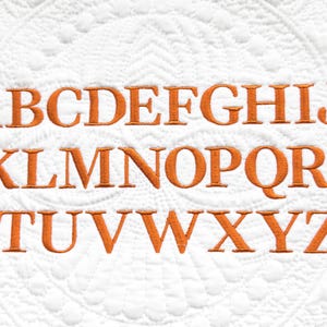 May include: An embroidered alphabet in a serif font, in a warm orange color, is displayed on a white quilted background. The letters A through Z are evenly spaced across the image, showcasing a classic and elegant design.