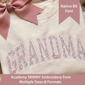 May include: A cream-colored crewneck sweatshirt featuring the word GRANDMA embroidered in a collegiate-style font. The letters are filled with a floral pattern in shades of pink and blue. A large dusty rose ribbon bow is attached to the top left.