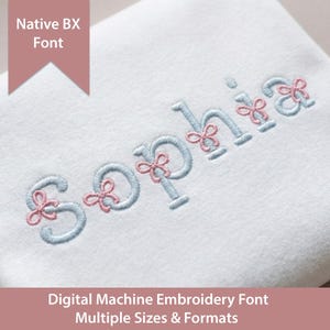 Può includere: Tessuto bianco ricamato con il nome "Sophia" in filo azzurro chiaro, accentuato da dettagli a fiocco rosa. È visibile anche il testo "Native BX Font" e "Digital Machine Embroidery Font Multiple Sizes & Formats".