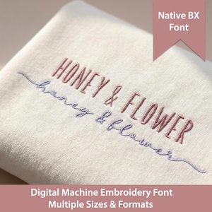 Op de afbeelding: Een gevouwen off-white stof met machinaal borduurwerk met de tekst HONEY & FLOWER in een vetgedrukt oudroze lettertype en de tekst honey & flower in een kleiner, cursief, stoffig blauw lettertype. Een oudroze banner toont Native BX Font.