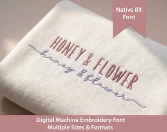 Puede incluir: Una tela de color blanco roto doblada con bordado a máquina que muestra el texto HONEY & FLOWER en una fuente rosa polvorienta y el texto honey & flower en una fuente cursiva azul más pequeña. Una pancarta rosa muestra Native BX Font.
