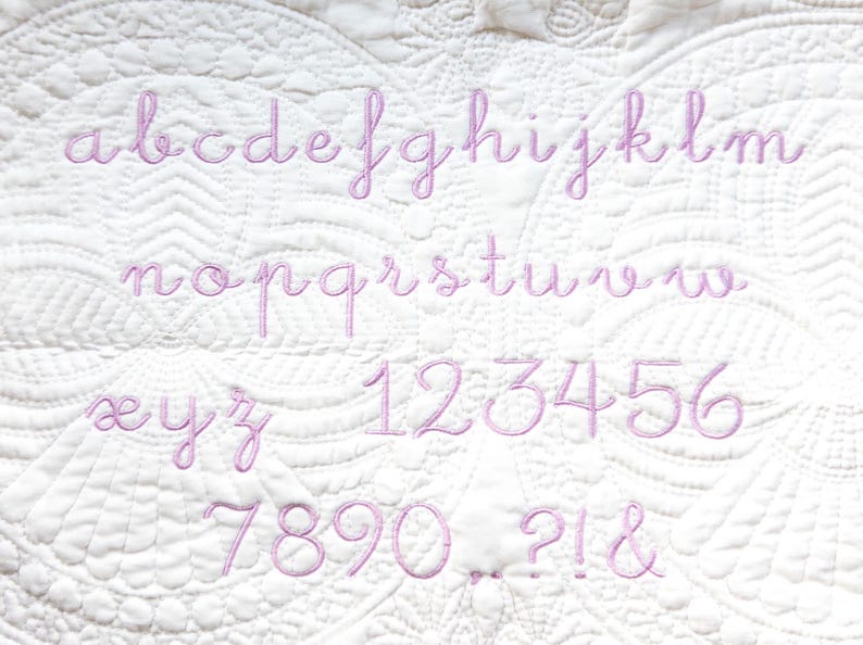 Peut inclure: Un tissu blanc avec un alphabet et des chiffres brod&eacute;s en rose. Les lettres sont en &eacute;criture cursive. Les chiffres sont dans une police similaire.