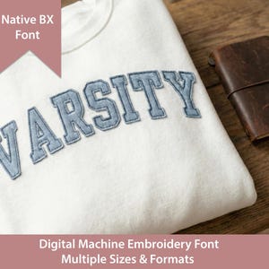 May include: A white sweatshirt with the word "VARSITY" embroidered in light blue. A brown leather notebook with a pen is next to the sweatshirt. The image also includes the text "Native BX Font" and "Digital Machine Embroidery Font Multiple Sizes & Formats."