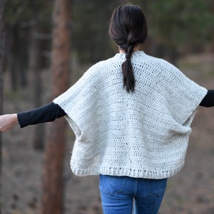 May include: A white crocheted cardigan with a loose fit and a slightly cropped length. The cardigan has a simple design with a wide, open neckline and long sleeves.