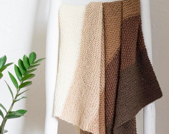 May include: A knitted throw blanket in shades of beige, brown, and cream. The blanket is draped over a white ladder.