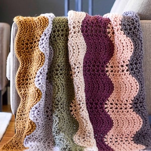May include: A multi-coloured crocheted blanket with a wavy pattern. The blanket is made in shades of mustard yellow, light purple, olive green, burgundy, and light pink.