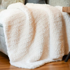 May include: A white fluffy blanket draped over a sofa with a wooden side table next to it.