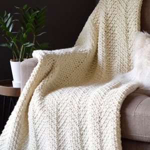 May include: A white crocheted throw blanket with a chevron pattern is draped over a brown armchair. The blanket has a scalloped edge.