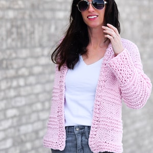 May include: A pink knitted cardigan with a v-neck and long sleeves. The cardigan is open in the front and has a relaxed fit.