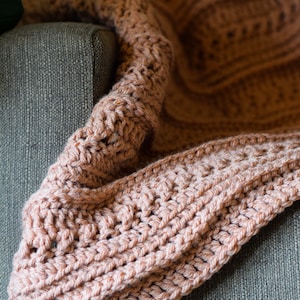 May include: A soft, light brown crocheted throw blanket draped over a gray couch.