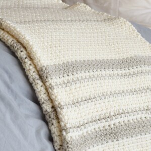 May include: A white and beige striped crocheted throw blanket draped over a bed.